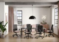 Biuro z drewnianą podłogą w którym stoją czarne fotele biurowe skill z różowymi siedziskami przy czarnym biurku